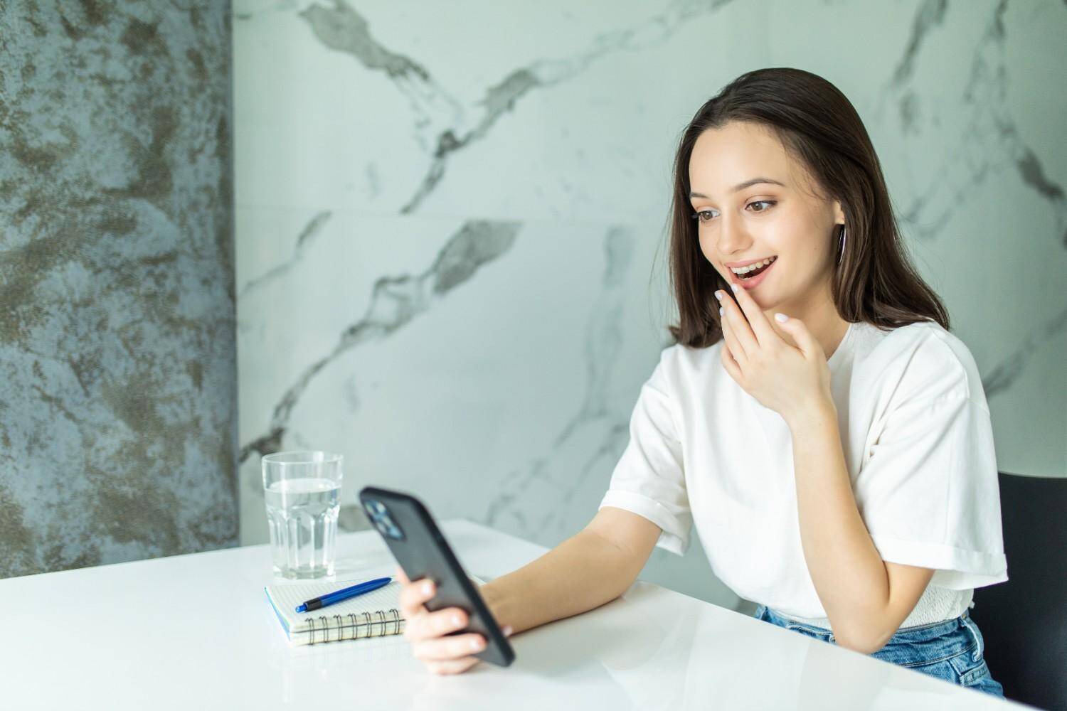 Woman smiling while checking her phone at a table.