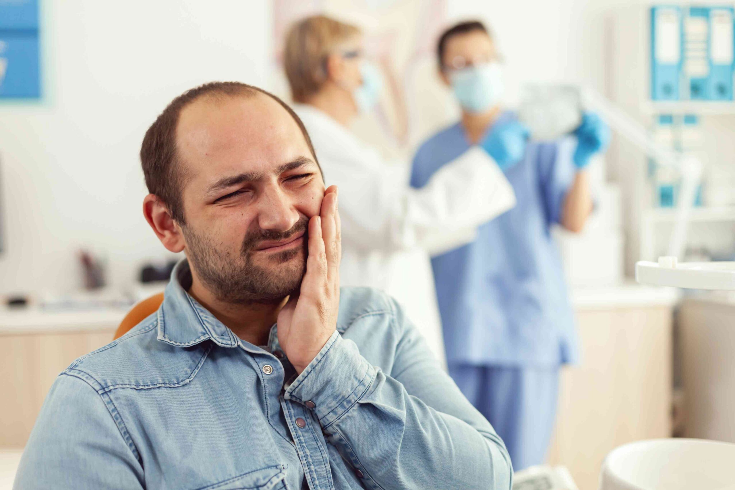 Man holding his jaw with a toothache in a dental office.